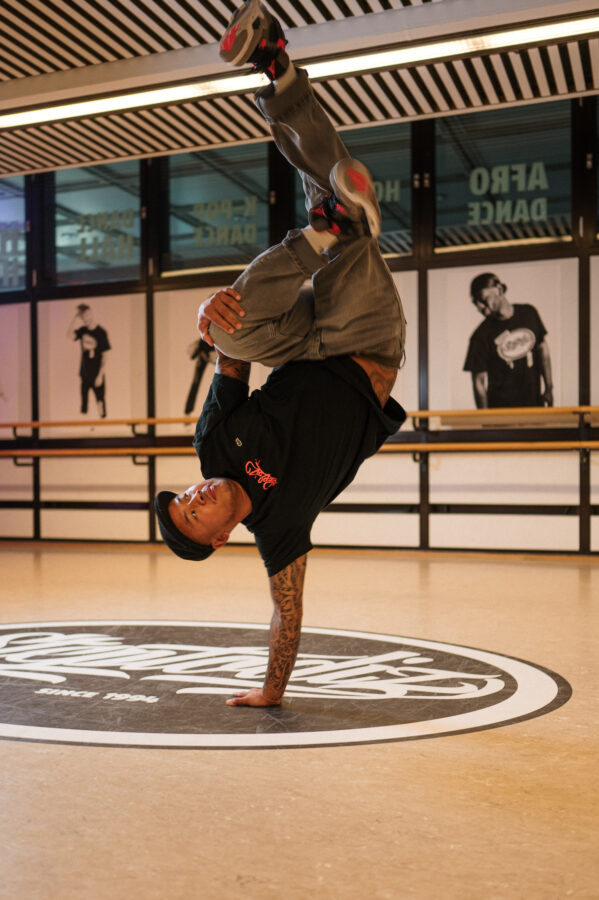 Ein Breakdancer, wie er auf einem Arm einen Handstand macht mit angewinkelten Beinen.