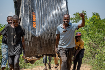 Mehrere Kenianer tragen einen vom Verein Maisha Bora e.V. gekauften Wassertank auf einem steinigen Weg zu seinem Bestimmungsort.