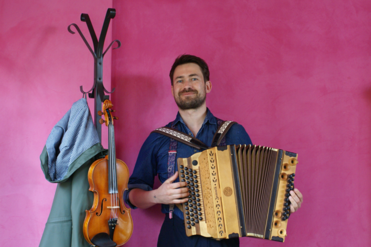 Johannes Sift, Musiker, mit einer Harmonika vor einer pinken Wand.