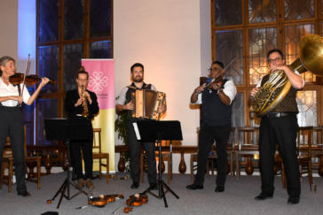 Eine Band mit Streich- und Blasinstrumenten, bestehend aus fünf Personen, steht auf einer Bühne.